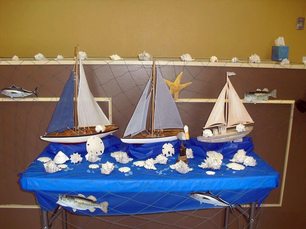 Maquettes de voiliers posées sur une table décorée d'un bleu pétant, avec coquillages et faux poissons.