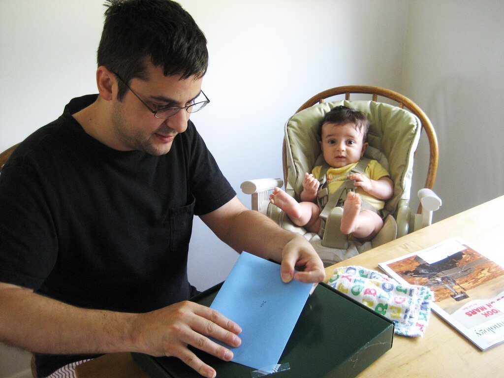 Jeune père qui ouvre ses cadeaux de fête des pères, avec son jeune enfant à côté