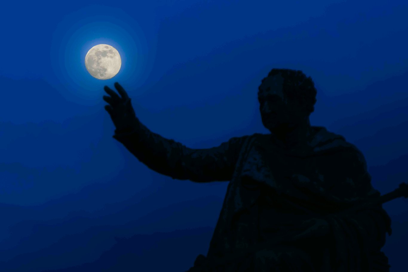 Silhouette d’une statue tendant la main vers la lune.